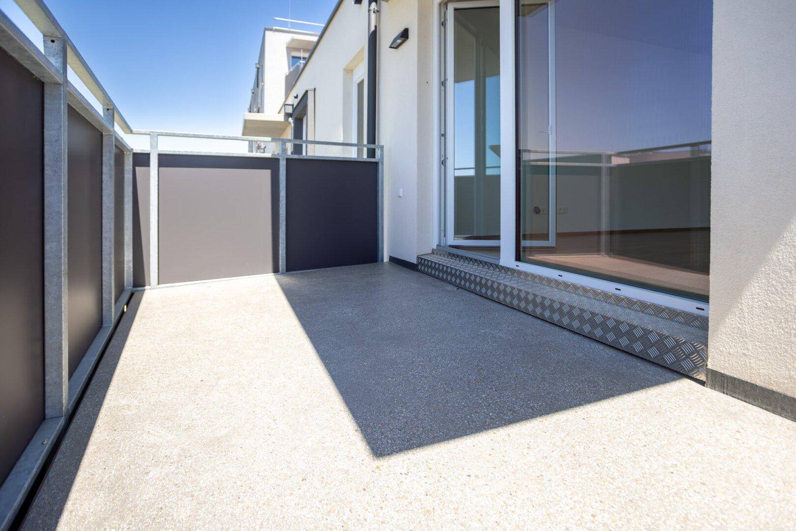 Heller Balkon mit Betonboden und Zugang zum Innenbereich durch eine Glasschiebetür.