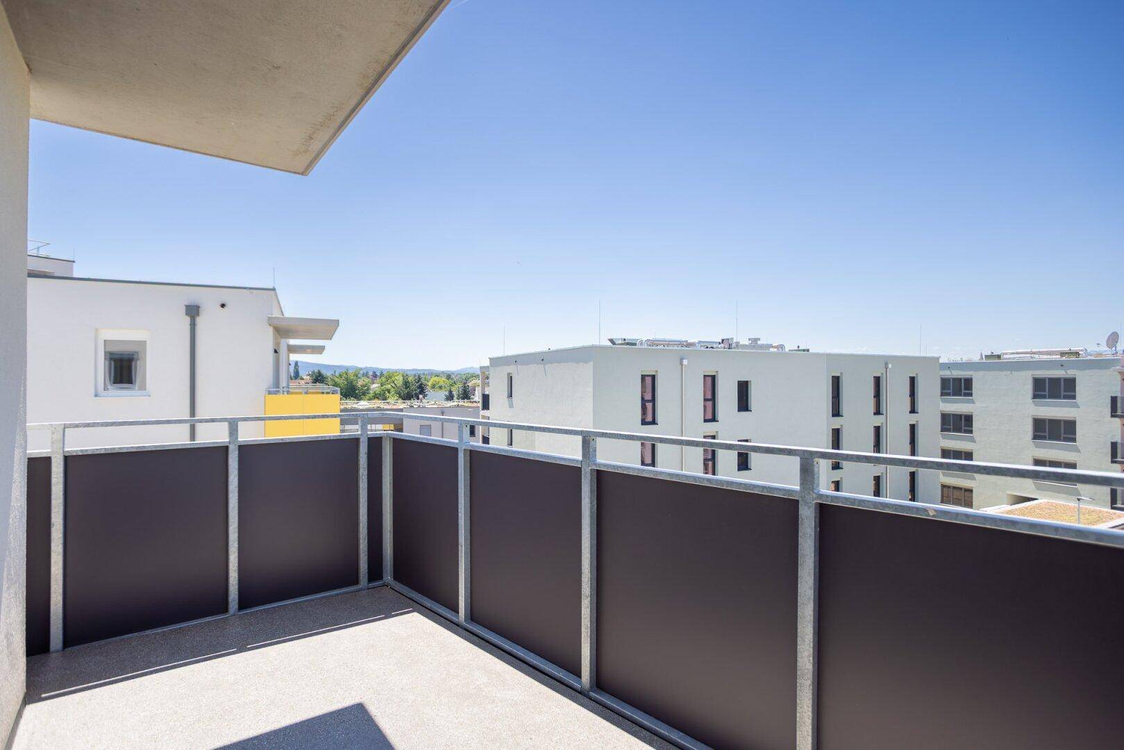 Sonniger Balkon mit Weitblick über die Stadt und grüne Umgebung.