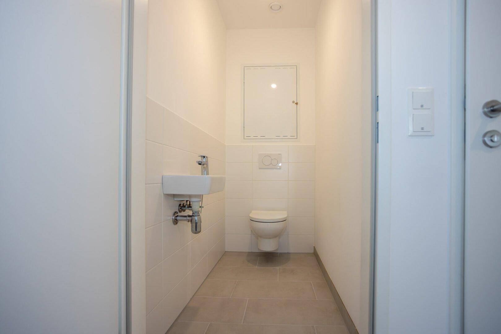 Kleines Gäste-WC mit weißen Fliesen, Toilette und einem kompakten Waschbecken.
