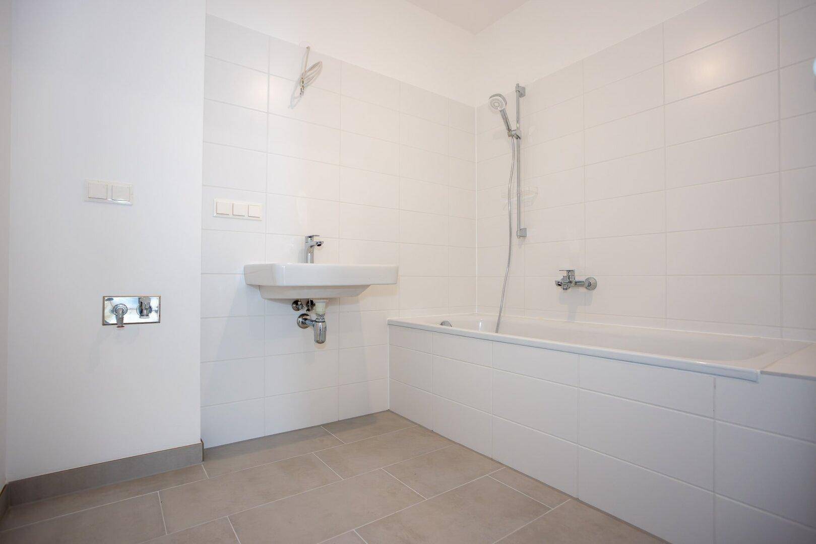 Modernes Badezimmer mit weißen Fliesen, Badewanne mit Duschfunktion und Einzelwaschbecken.