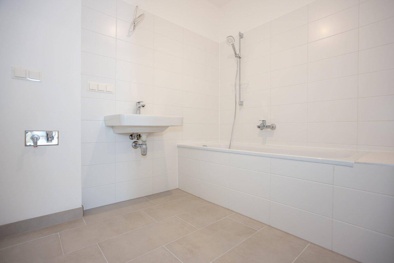 Modernes Badezimmer mit weißen Fliesen, Badewanne mit Duschfunktion und Einzelwaschbecken.