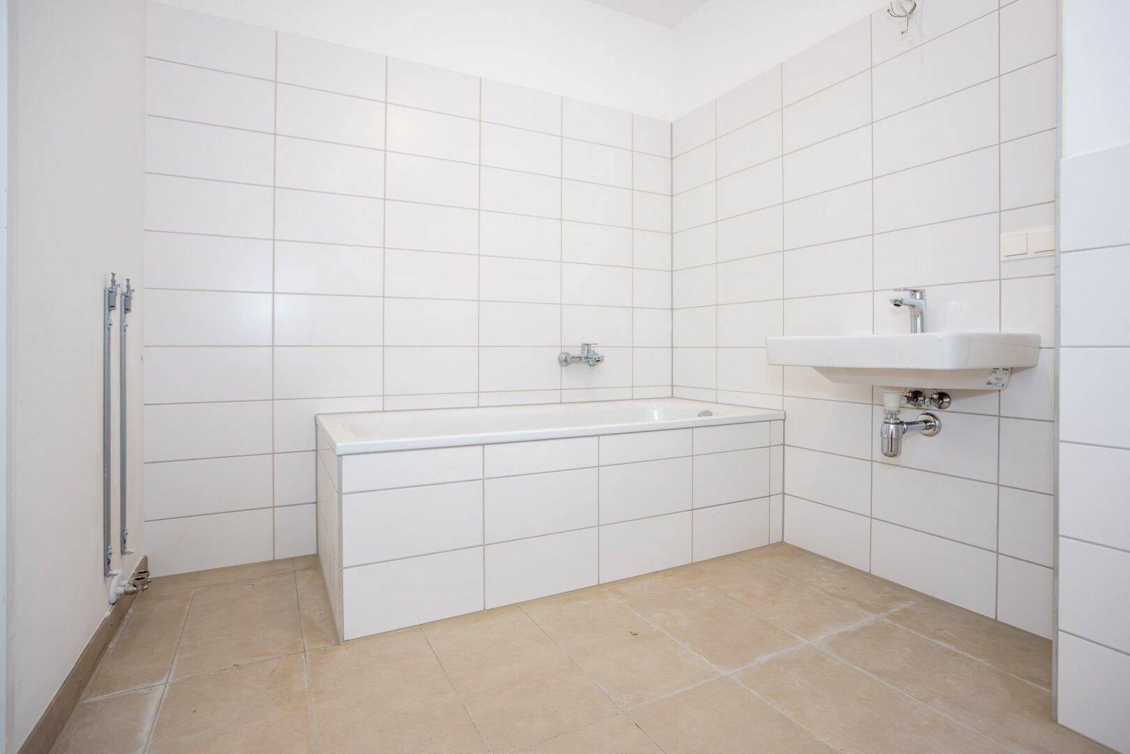 Modernes Badezimmer mit weißen Fliesen, Badewanne und Einzelwaschbecken in einem Neubau.