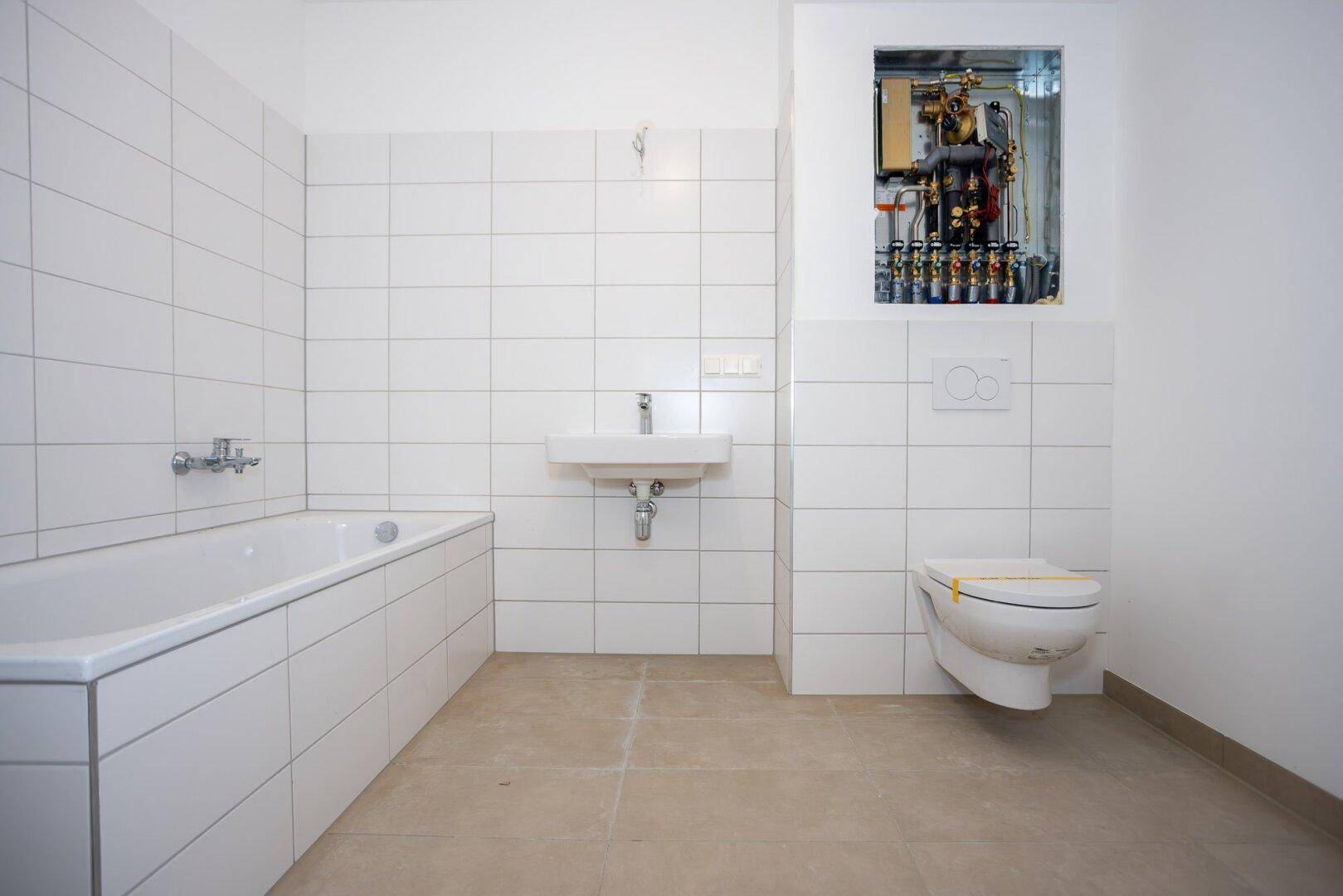 Helles Badezimmer mit Badewanne, WC und Waschbecken, teilweise gefliest in einem Neubau.