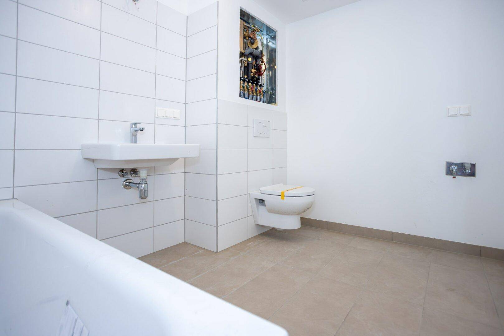 Sauberes Badezimmer mit weißen Wandfliesen, Badewanne und wandhängendem WC in einem Neubau.