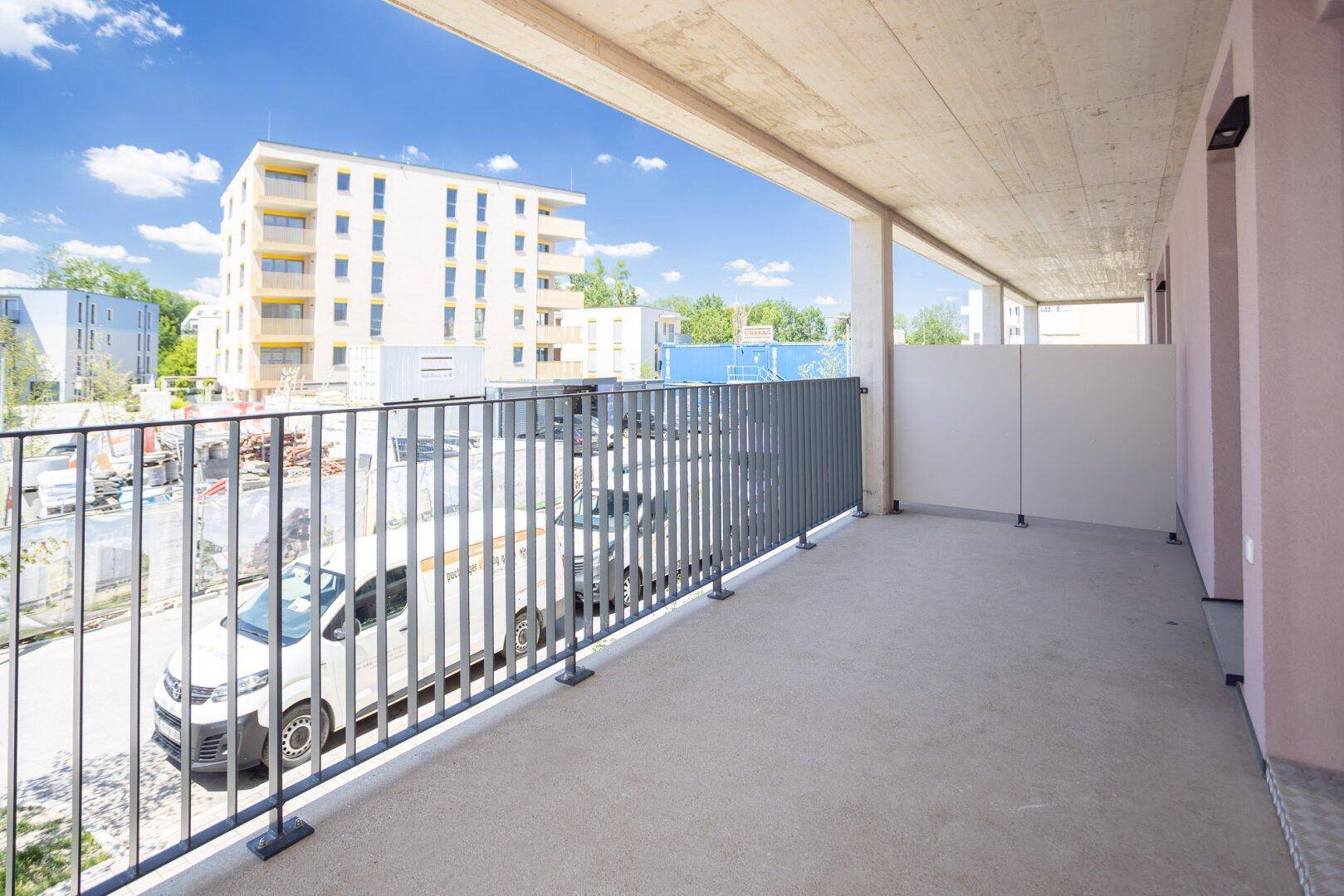 Geräumiger Balkon mit Metallgeländer und Blick auf die umliegenden Neubauten und die Stadt.