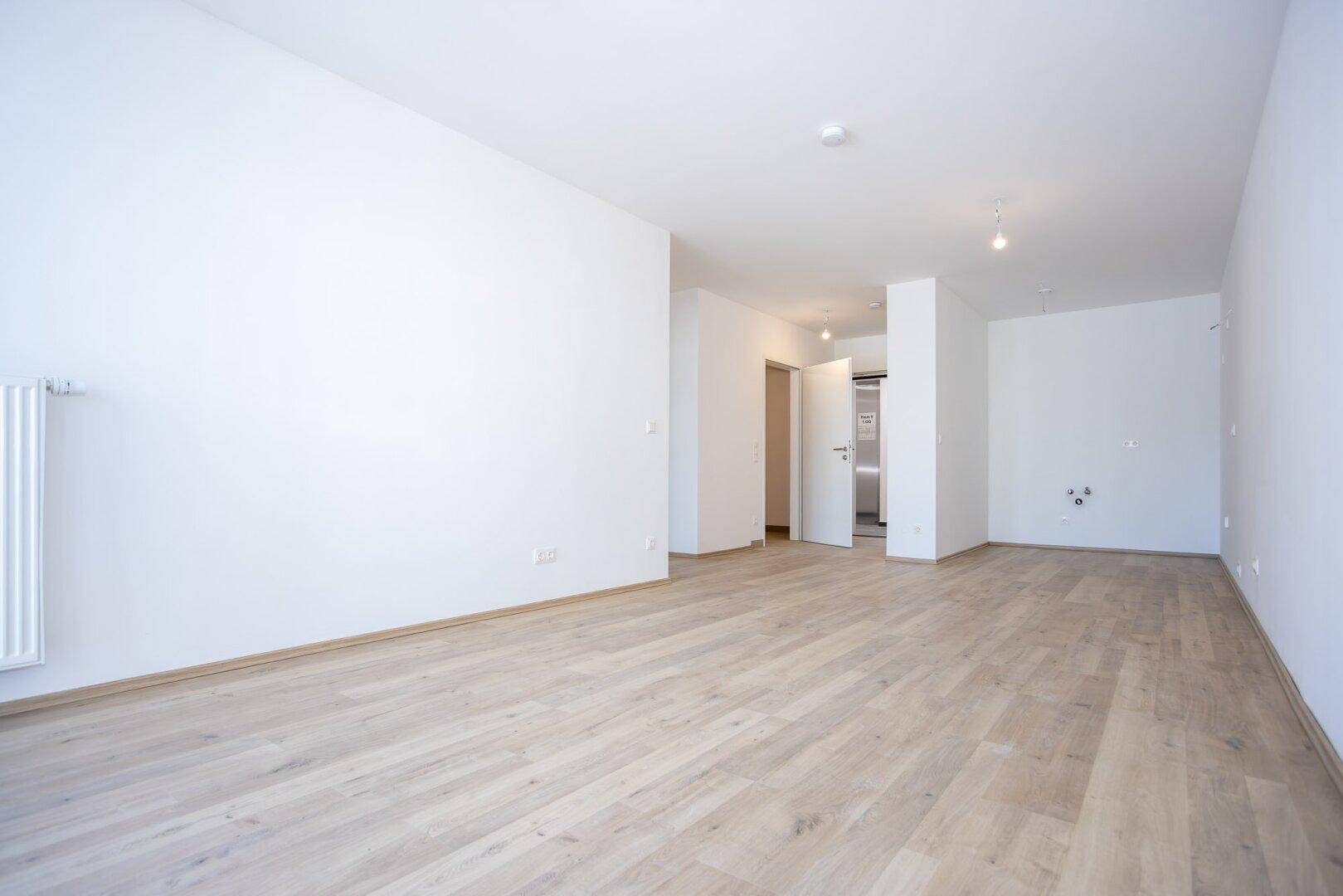Großes, helles Zimmer mit Laminatboden und Zugang zu weiteren Räumen in einem Neubau.