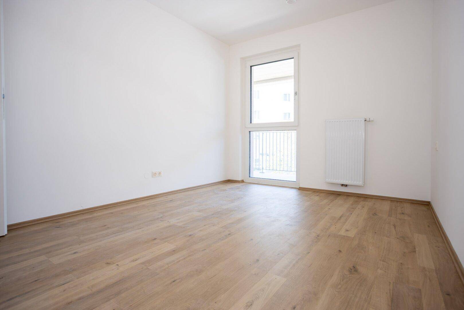 Unmöbliertes Schlafzimmer mit Laminatboden und großem Fenster für viel Tageslicht in einem Neubau.