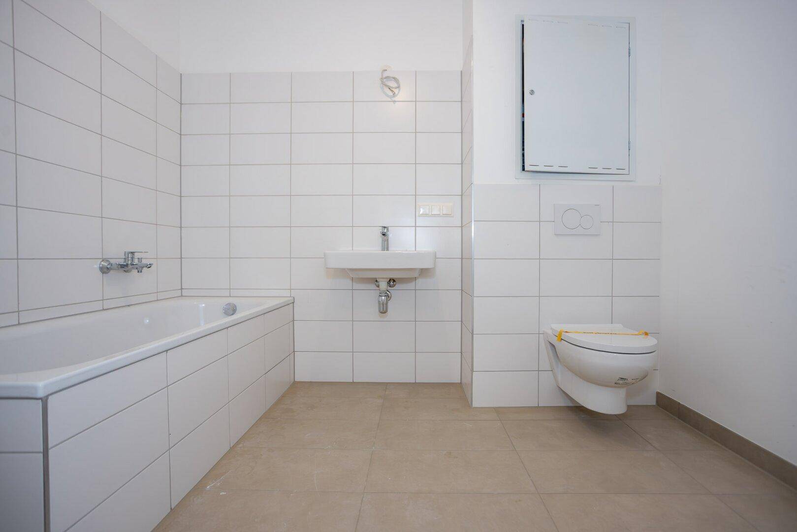 Modernes Badezimmer mit Badewanne, Waschbecken, wandhängendem WC und weißen Fliesen an den Wänden.