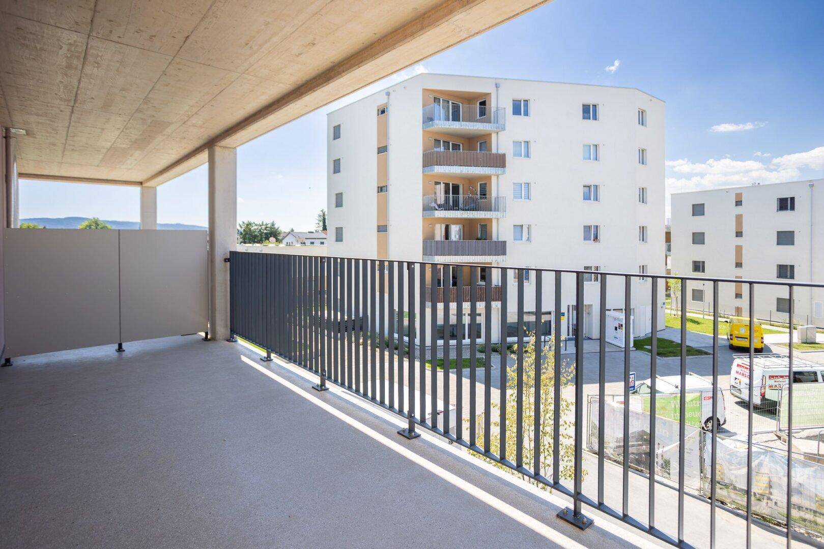 Geräumiger Balkon mit Metallgeländer und Blick auf moderne Wohngebäude unter blauem Himmel.