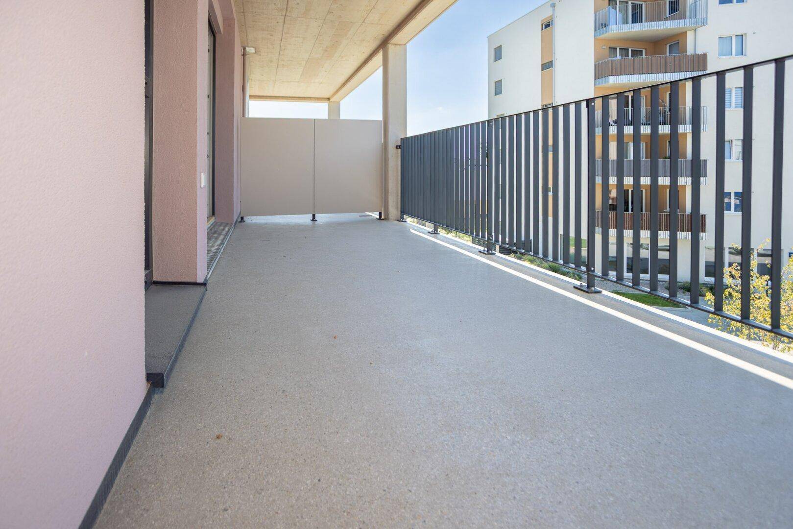 Breiter Balkon mit schlichtem Design und Blick auf die umliegenden Neubauten an einem sonnigen Tag.