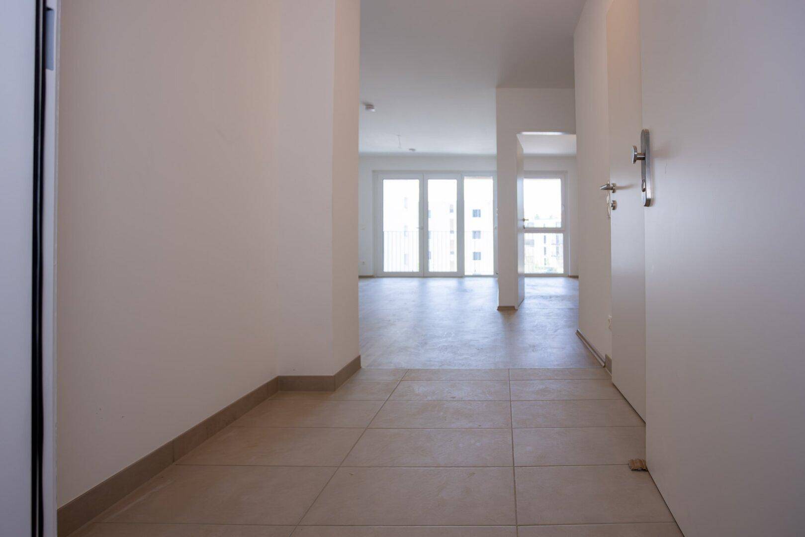Heller Eingangsbereich mit Fliesenboden, der zu den Wohnräumen führt, in einem Neubau.