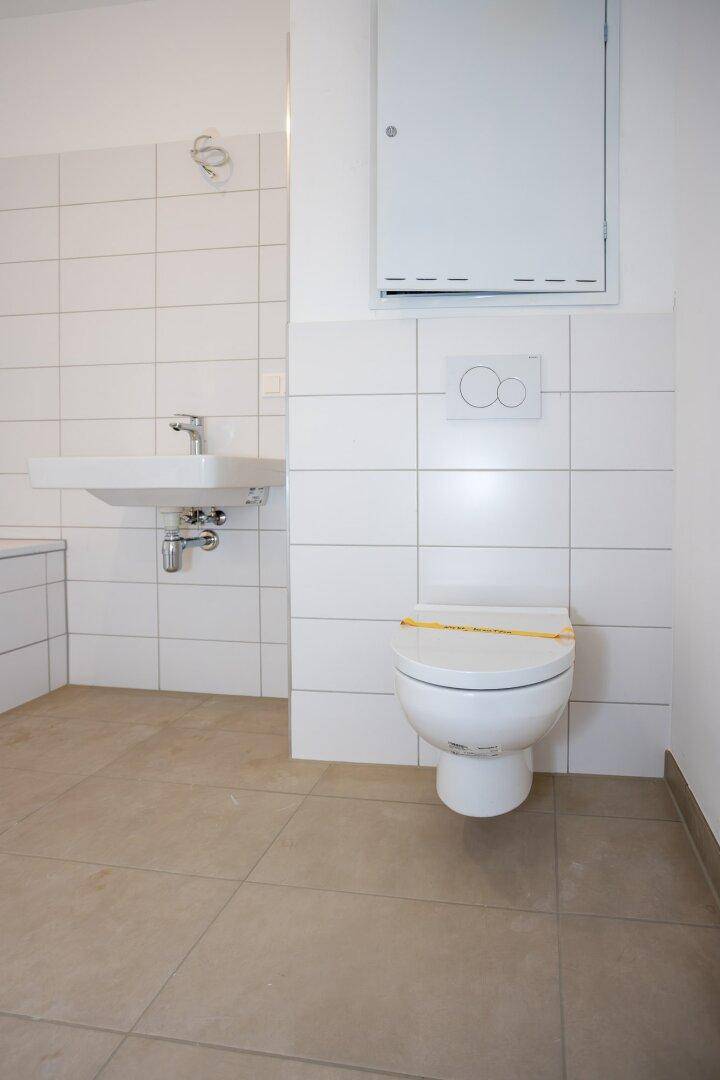 Funktionales Badezimmer mit WC, Waschbecken und weißen Fliesen an den Wänden, in neuwertigem Zustand.