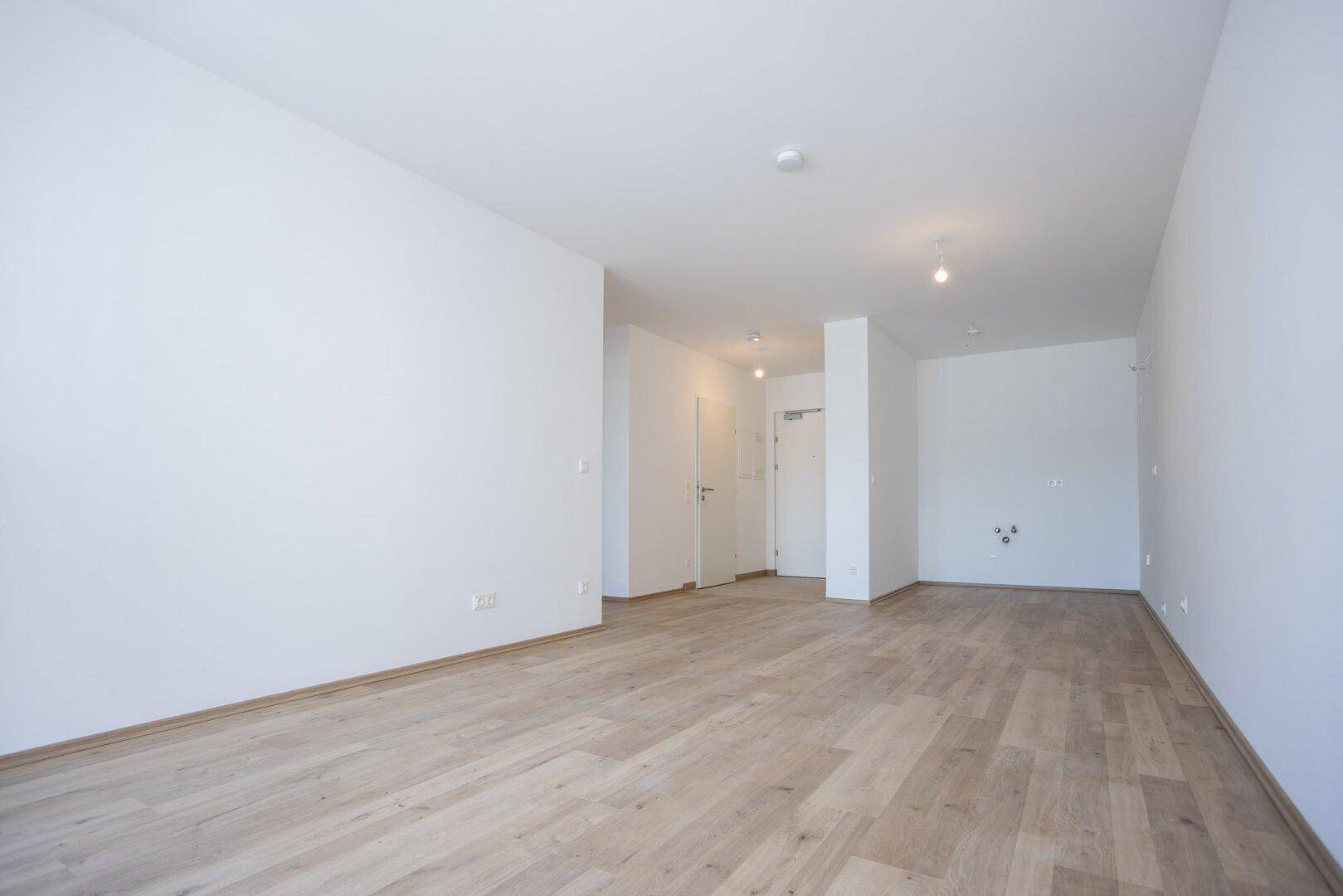Heller, unmöblierter Wohnbereich mit Laminatboden und weiß gestrichenen Wänden, bereit zum Einzug.