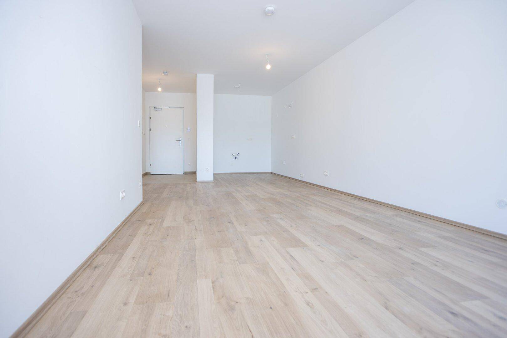 Geräumiger, leerer Wohnbereich mit hellem Laminatboden und weiß gestrichenen Wänden, ideal für individuelle Gestaltung.