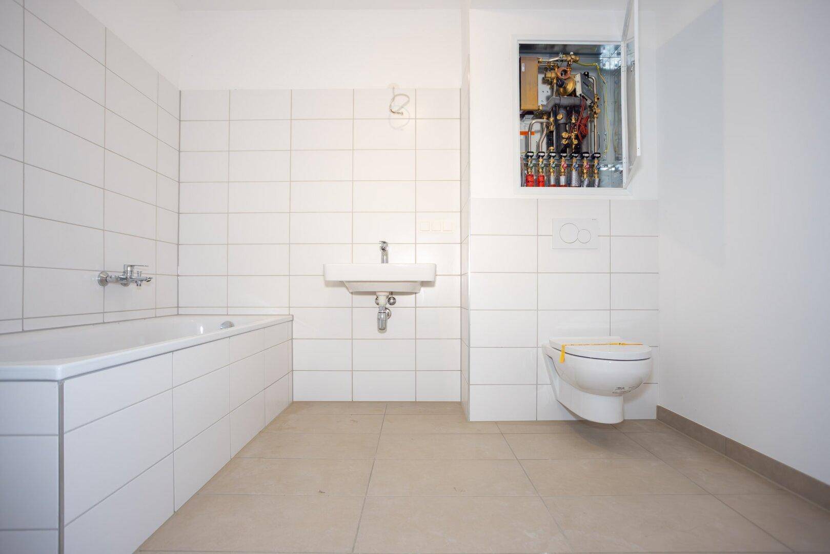 Modernes Badezimmer mit weißen Fliesen, Badewanne, wandhängendem WC und Waschbecken.