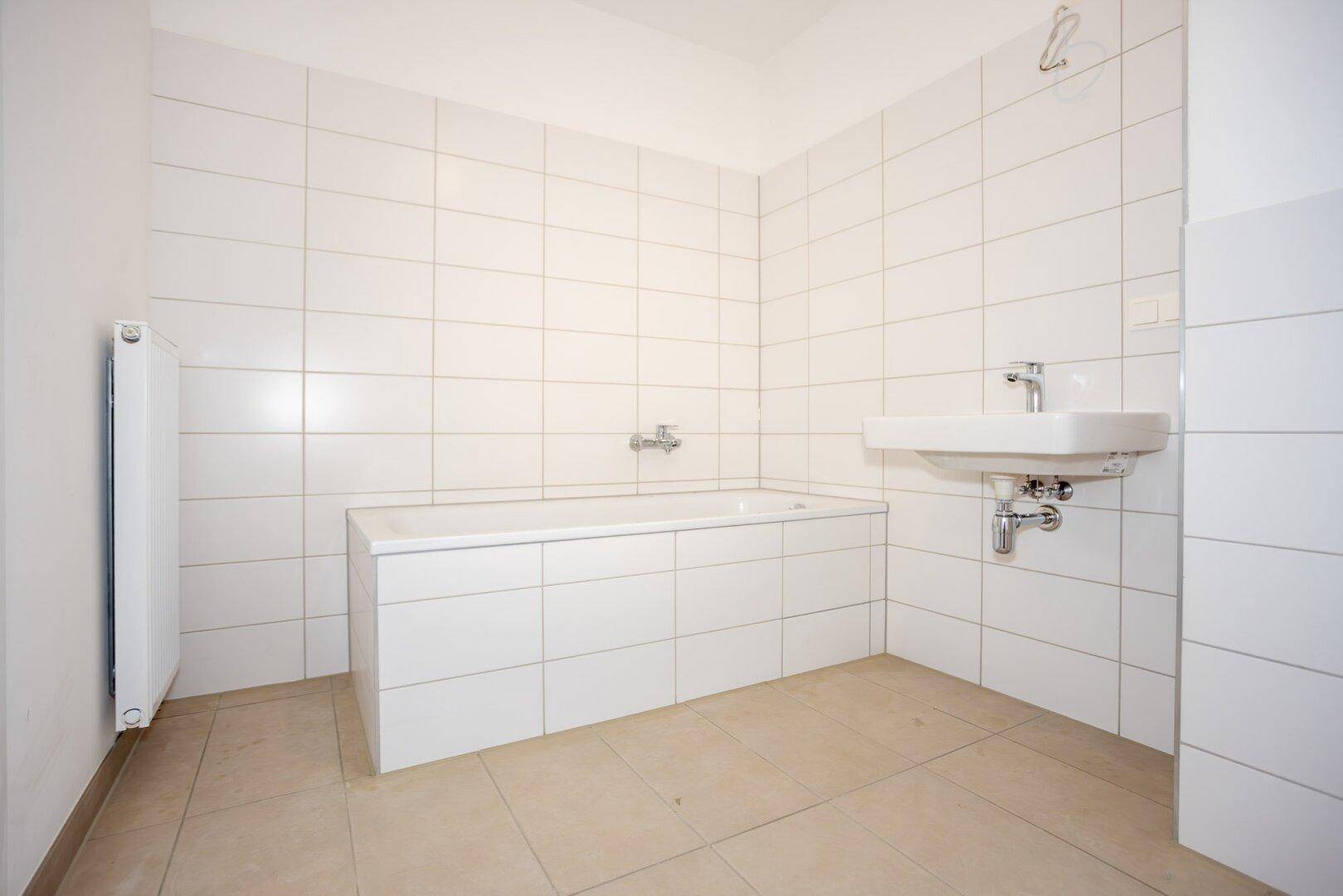 Helles Badezimmer mit Badewanne, Waschbecken und Heizkörper, in einem gepflegten Zustand.