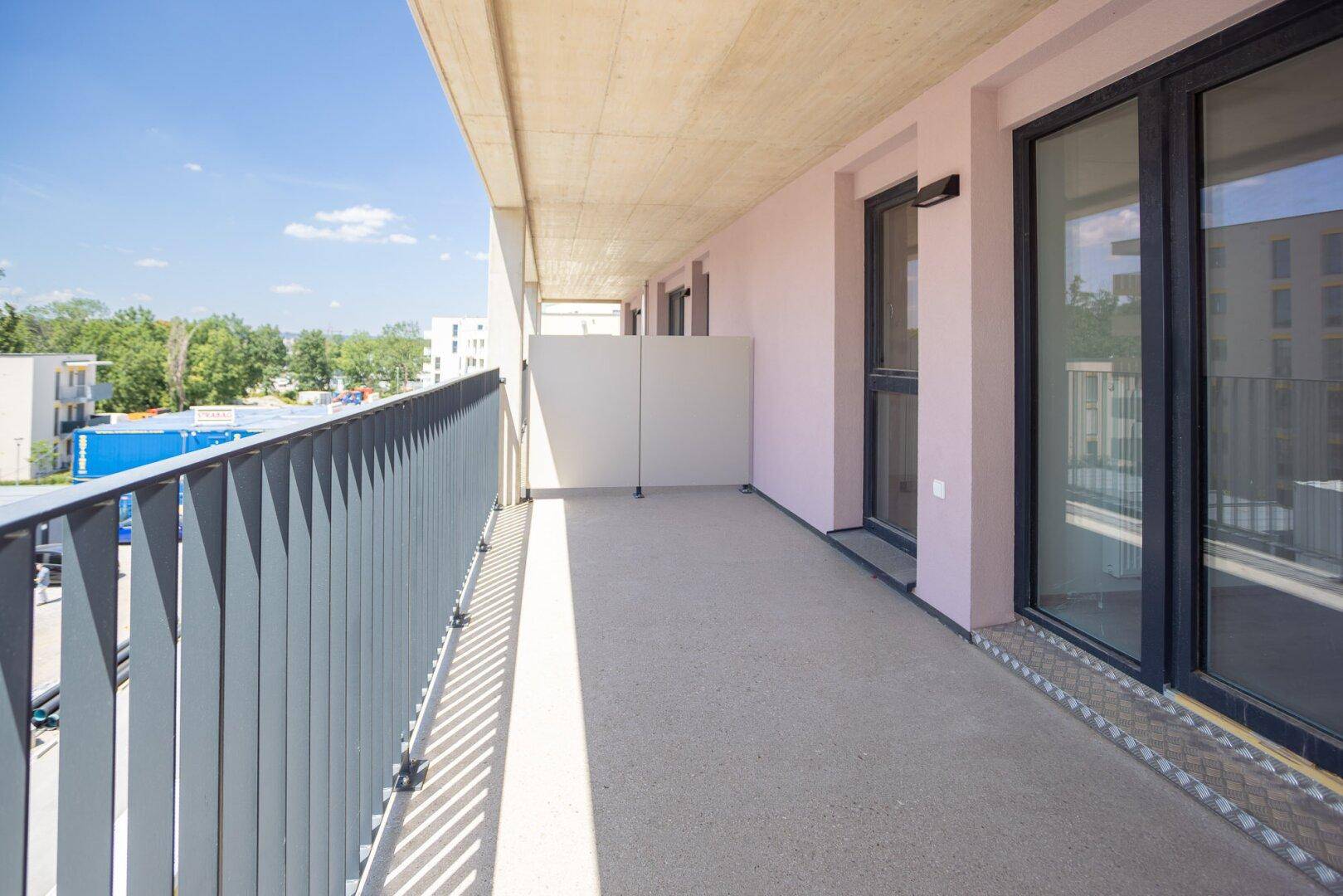 Langer Balkon mit moderner Brüstung und Zugang zu den hellen Innenräumen des Neubaus.