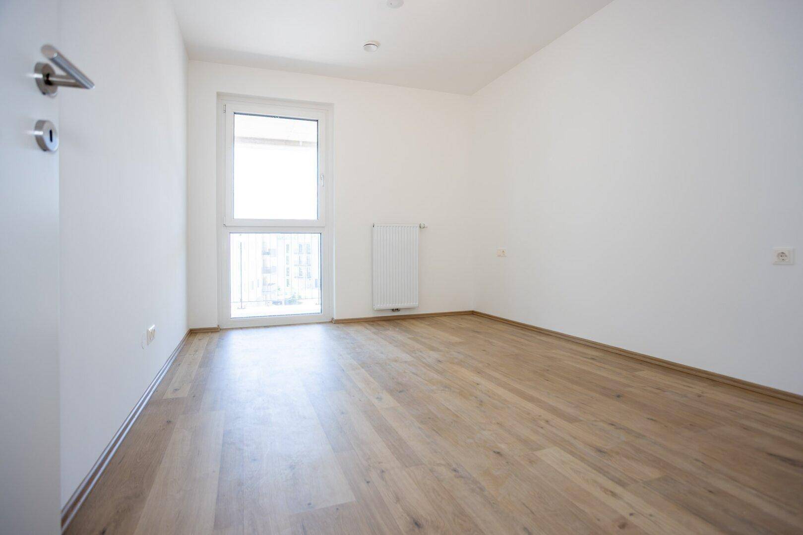Helles Schlafzimmer mit Laminatboden und einem großen Fenster, ideal für individuelle Einrichtung.