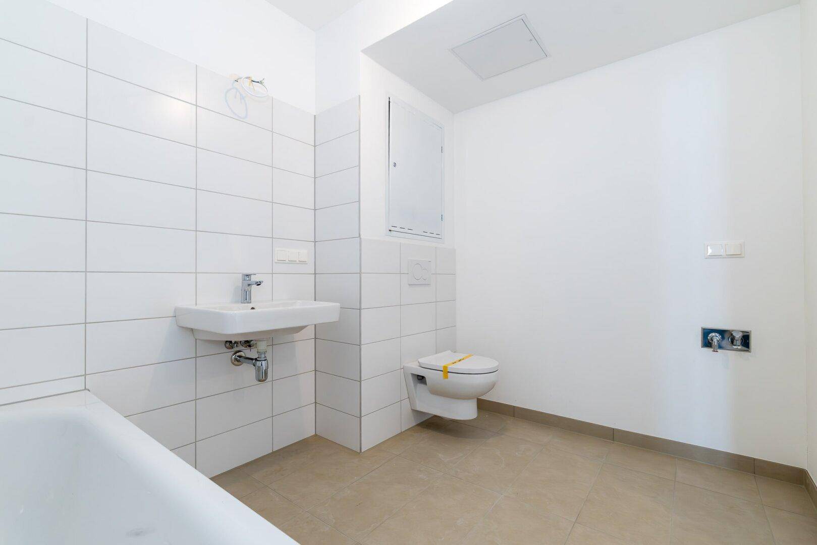 Helles Badezimmer mit Badewanne, WC und Waschbecken, ausgestattet mit weißen Fliesen.