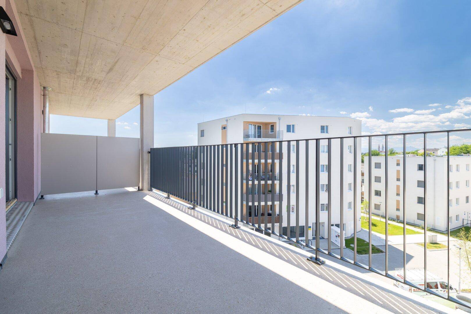 Großer Balkon mit Metallgeländer und Blick auf die umliegenden Neubauten.