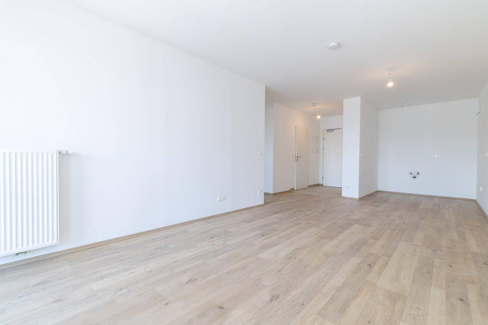Heller, unmöblierter Raum mit Laminatboden und Heizkörper, ideal als Wohnbereich.