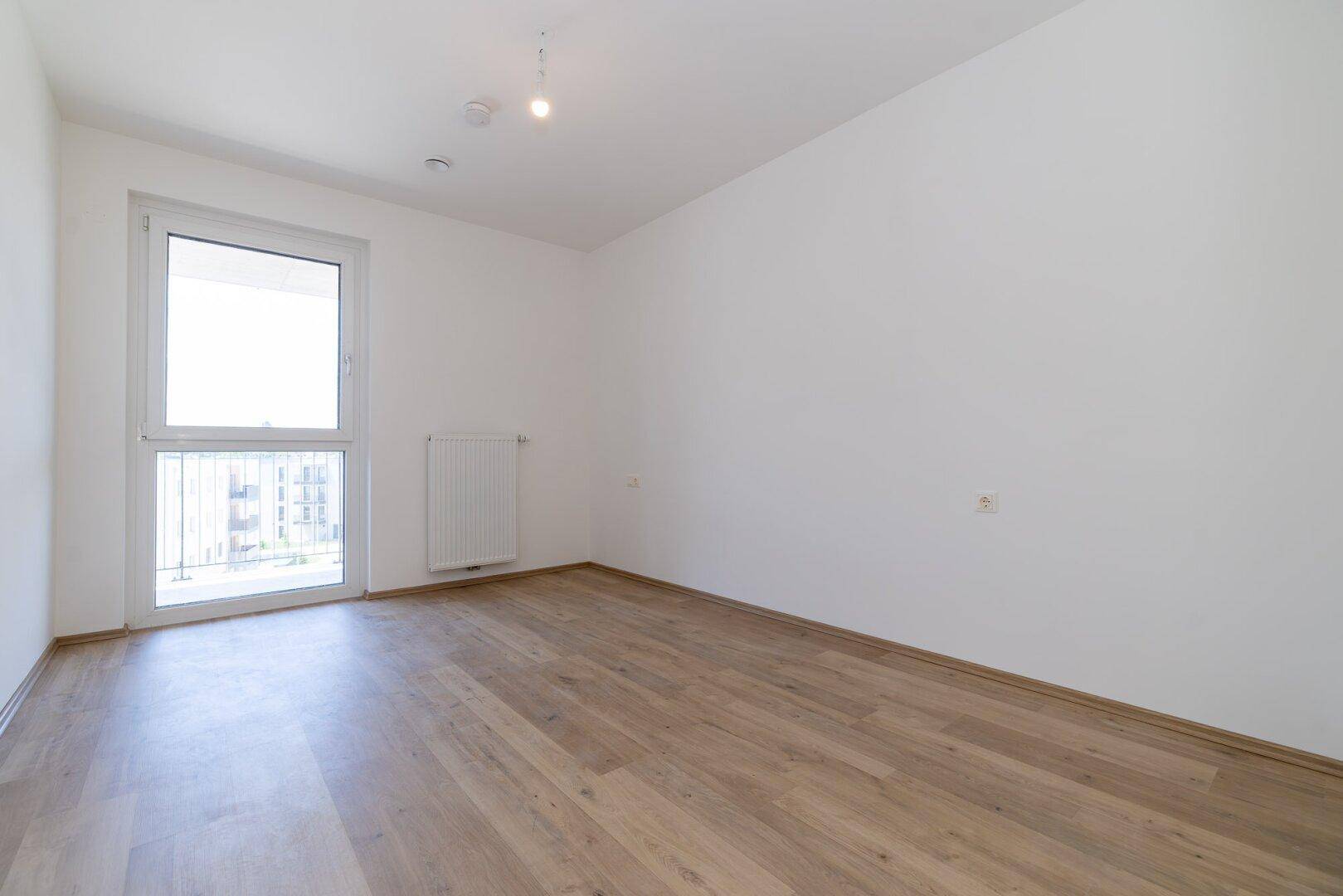 Helles Schlafzimmer mit Laminatboden und Zugang zu einem französischen Balkon.