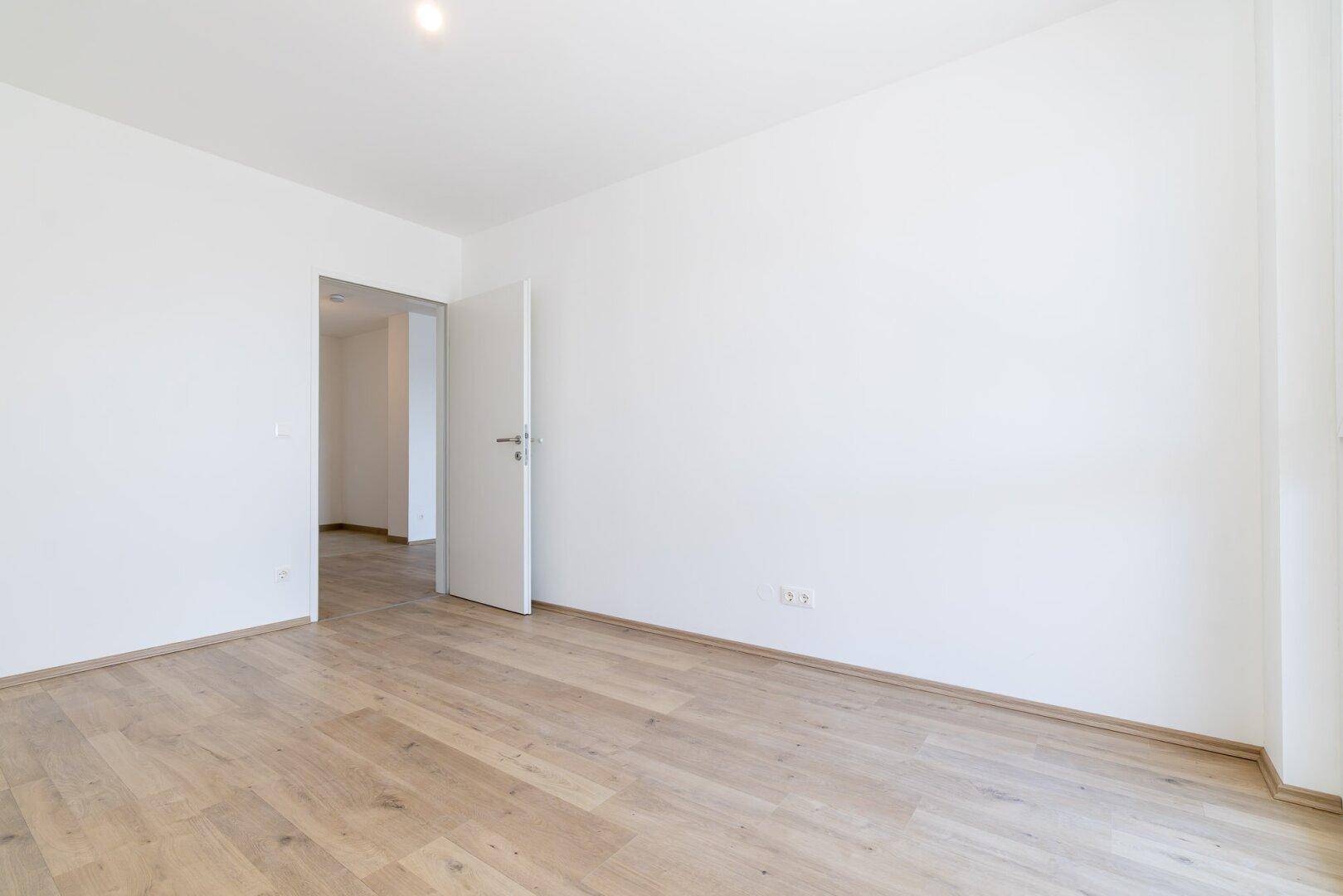 Leerer Raum mit hellem Laminatboden und weiß gestrichenen Wänden, vielseitig nutzbar.