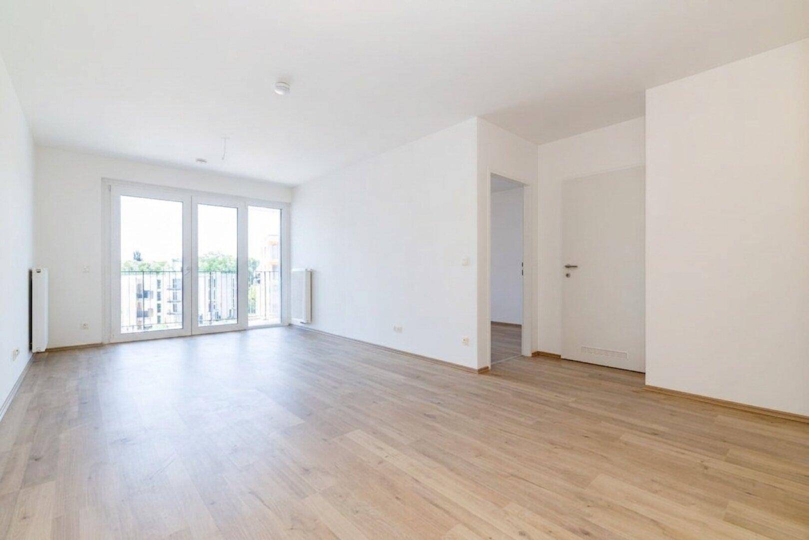 Geräumiges Wohnzimmer mit großen Fenstern und hellem Laminatboden, bereit zum Einzug.