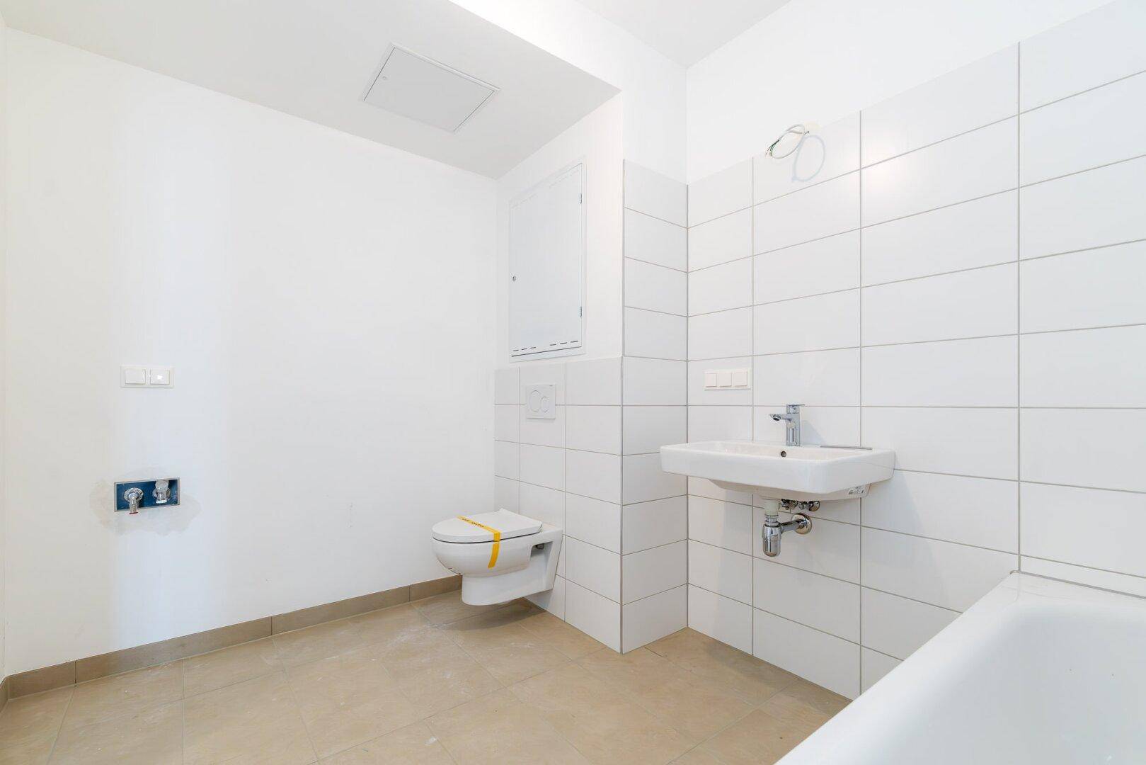 Helles Badezimmer mit weißen Wandfliesen, Badewanne und WC, bereit für die erste Nutzung.