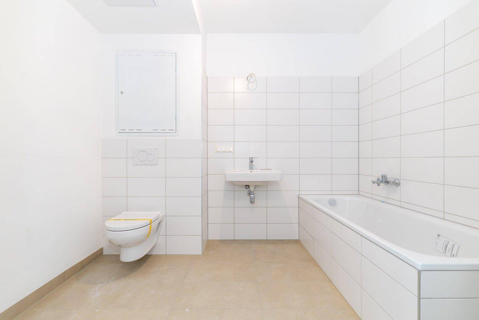 Modernes Badezimmer mit weißen Fliesen, Badewanne, WC und Waschbecken, in neuwertigem Zustand.
