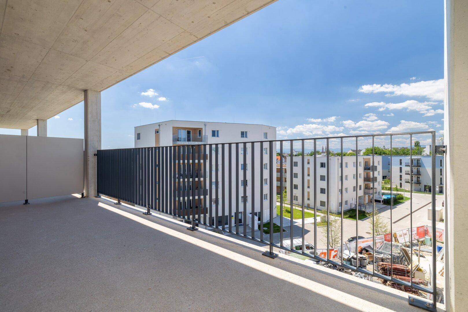 Balkon mit Blick auf die umliegenden Neubauten und die grüne Umgebung unter blauem Himmel.