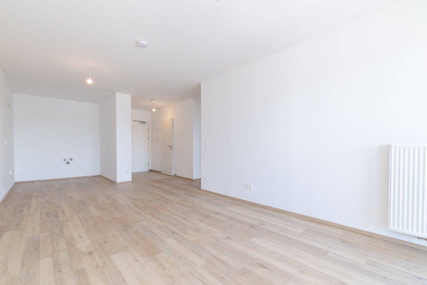 Leerer Küchenbereich mit Laminatboden und vorbereiteten Anschlüssen, bereit für eine individuelle Gestaltung.