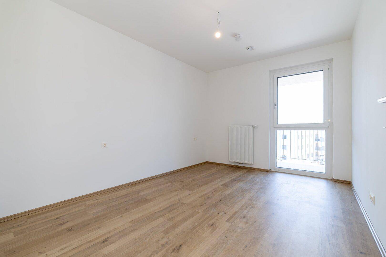 Helles Schlafzimmer mit Laminatboden und Fenster mit Balkonzugang, bietet eine ruhige Atmosphäre.
