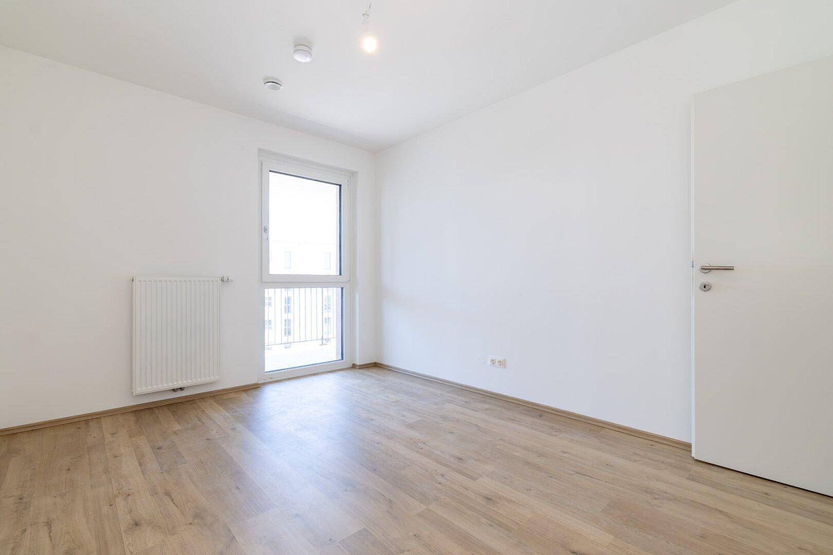 Freundliches Schlafzimmer mit Laminatboden und großem Fenster, ideal für erholsame Nächte.