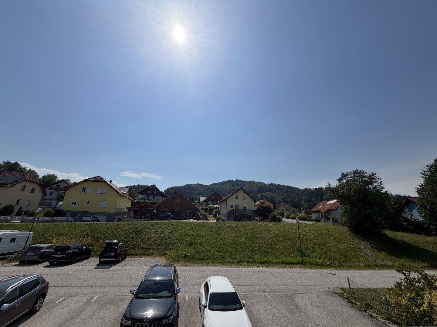 Weitläufiger Blick über die Nachbarschaft mit Häusern, Parkplätzen und grünen Hügeln unter strahlendem Himmel.