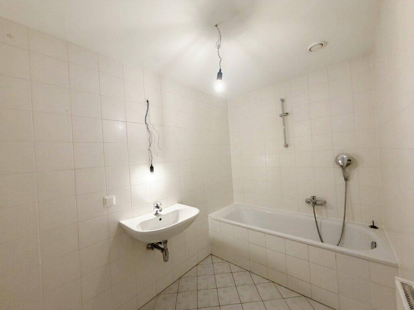 Modern gefliestes Badezimmer mit weißer Badewanne, Wandwaschbecken und hellen Fliesen.