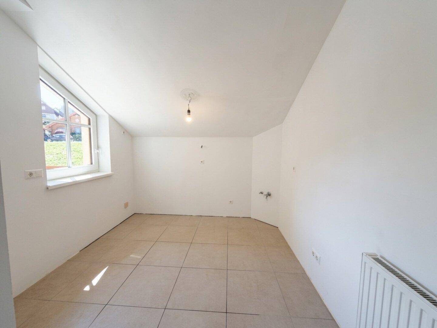 Dachzimmer mit Fliesenboden, weißen Wänden und einem Fenster, das viel Tageslicht hereinlässt.