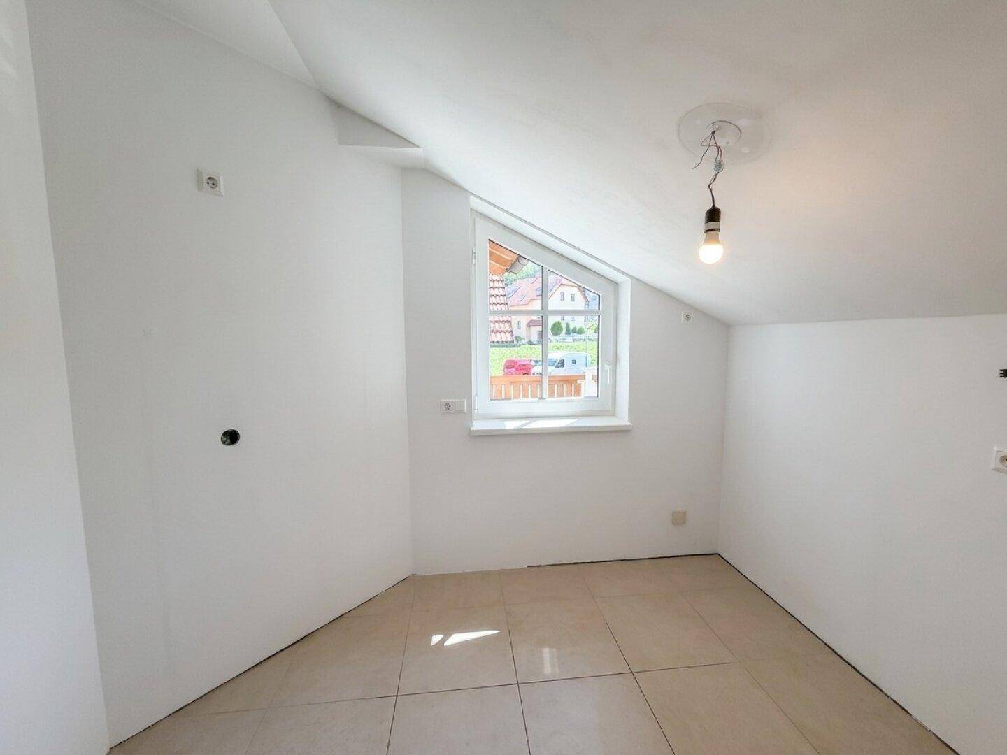 Helles Dachzimmer mit Fliesenboden, weißen Wänden und einem schrägen Fenster.