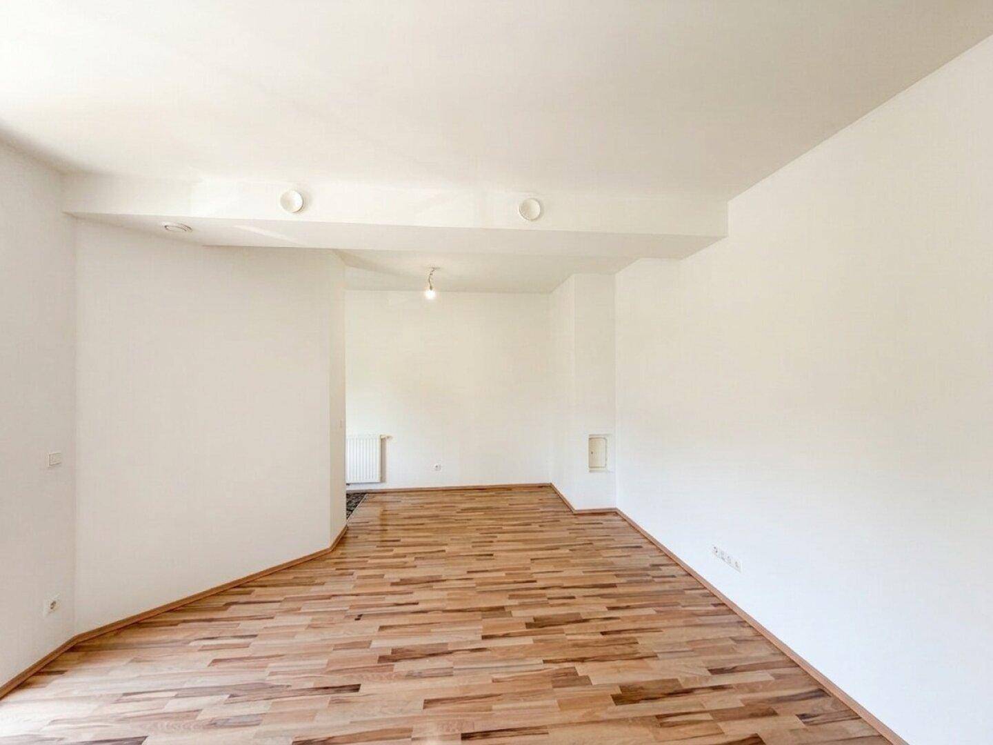 Geräumiger, heller Raum mit Laminatboden und weißen Wänden, ideal für Wohn- oder Essbereich.