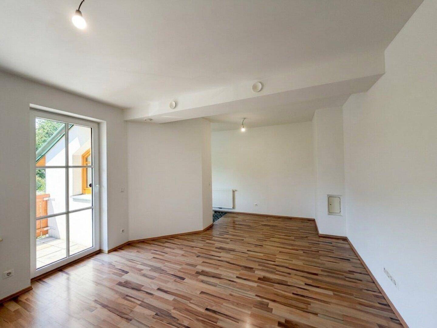 Heller Wohnbereich mit Laminatboden, weißen Wänden und einer Tür, die ins Freie führt.