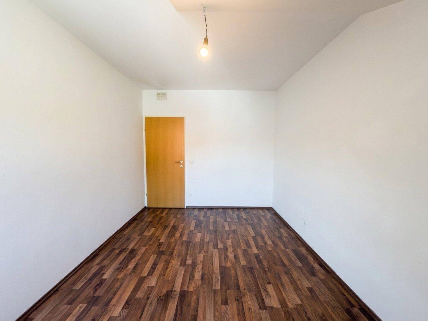 Geräumiges Dachzimmer mit dunklem Laminatboden und weißen Wänden, bereit zur Einrichtung.