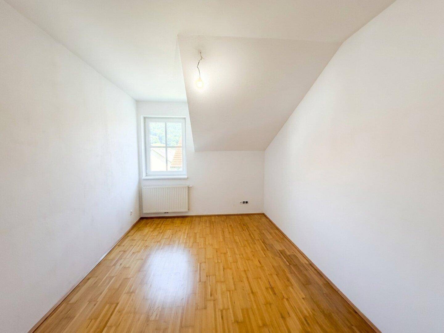 Helles Dachzimmer mit hellem Laminatboden, weißen Wänden und einem Fenster in der Dachschräge.