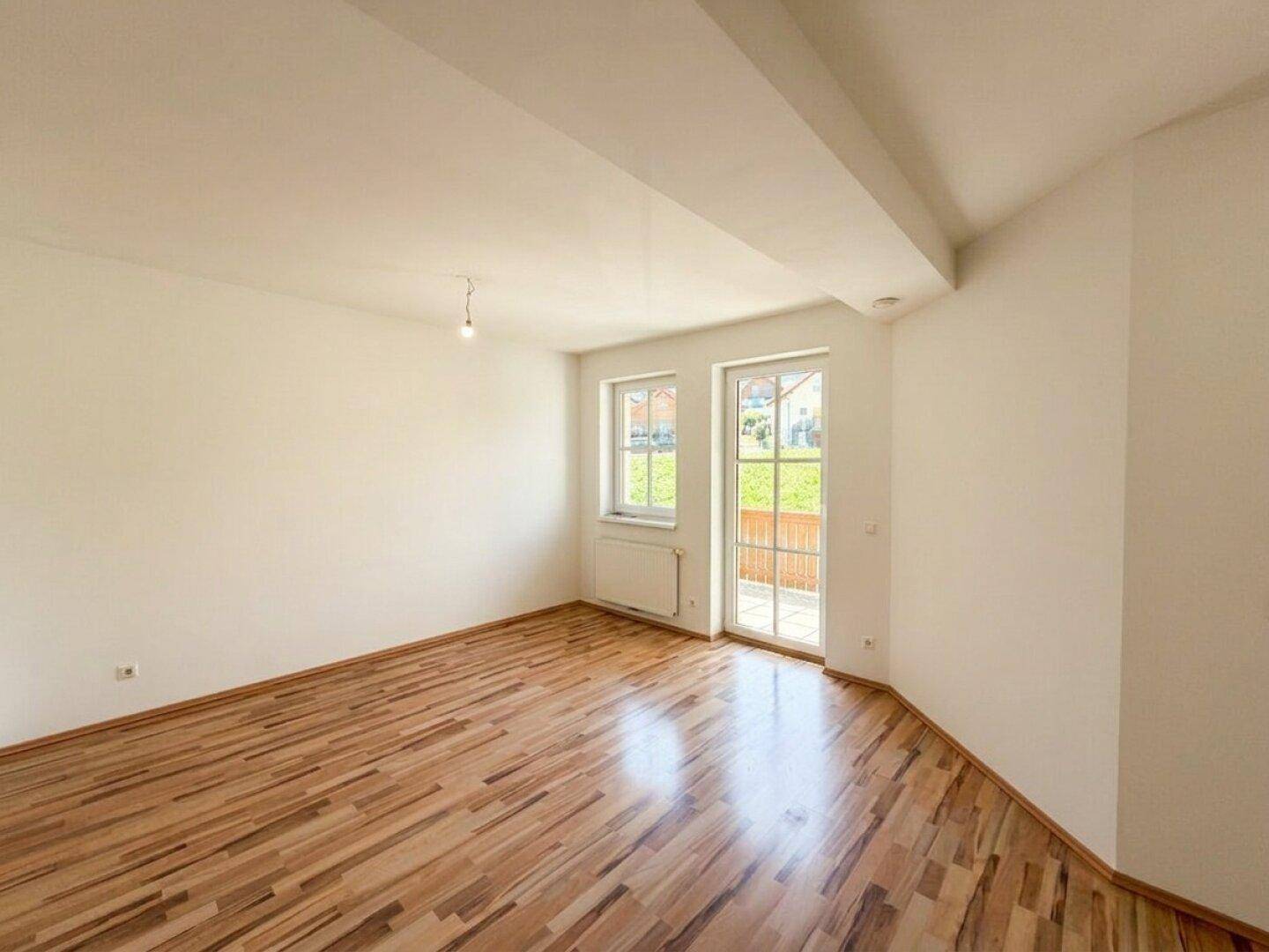 Lichtdurchfluteter Raum mit Laminatboden, weißen Wänden und direktem Zugang zum Außenbereich.