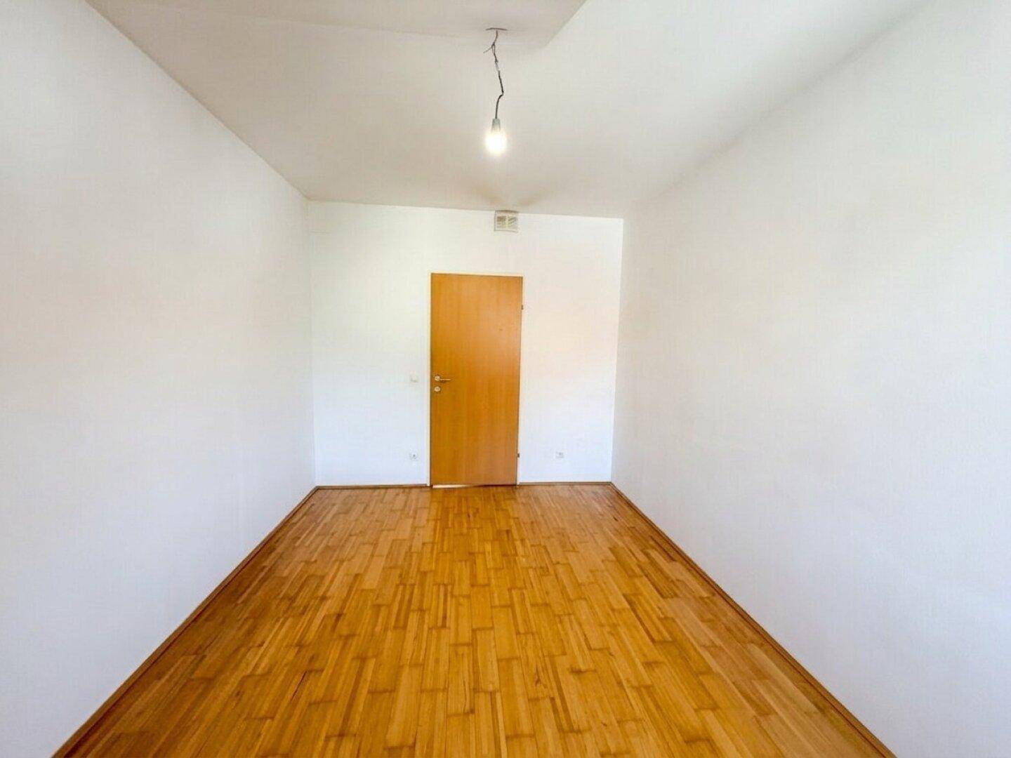 Dachzimmer mit hellem Laminatboden, weißen Wänden und einer Holztür, vielseitig nutzbar.