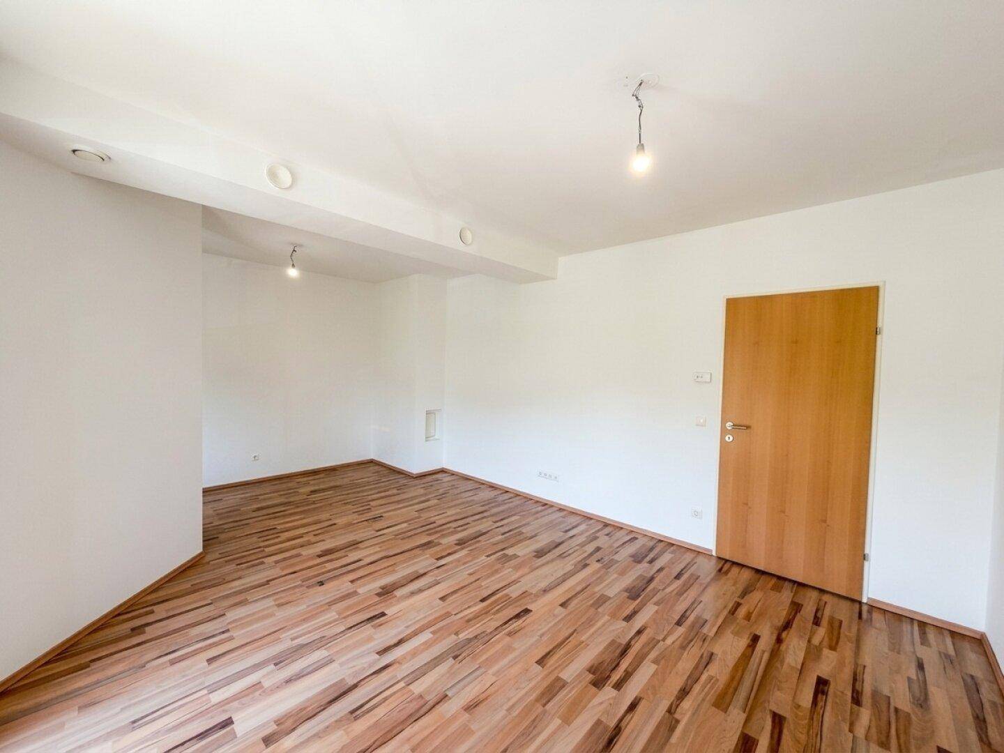 Unmöblierter Raum mit Laminatboden, weißen Wänden und einer Holztür, bereit zur individuellen Gestaltung.