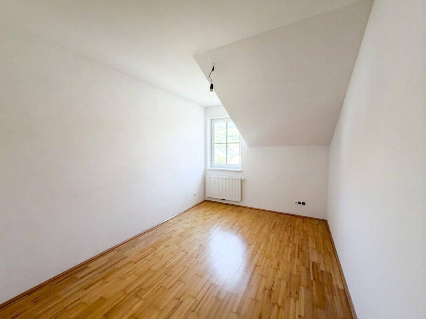 Lichtdurchflutetes Dachzimmer mit hellem Laminatboden und weißen Wänden, ideal für ein Kinderzimmer.