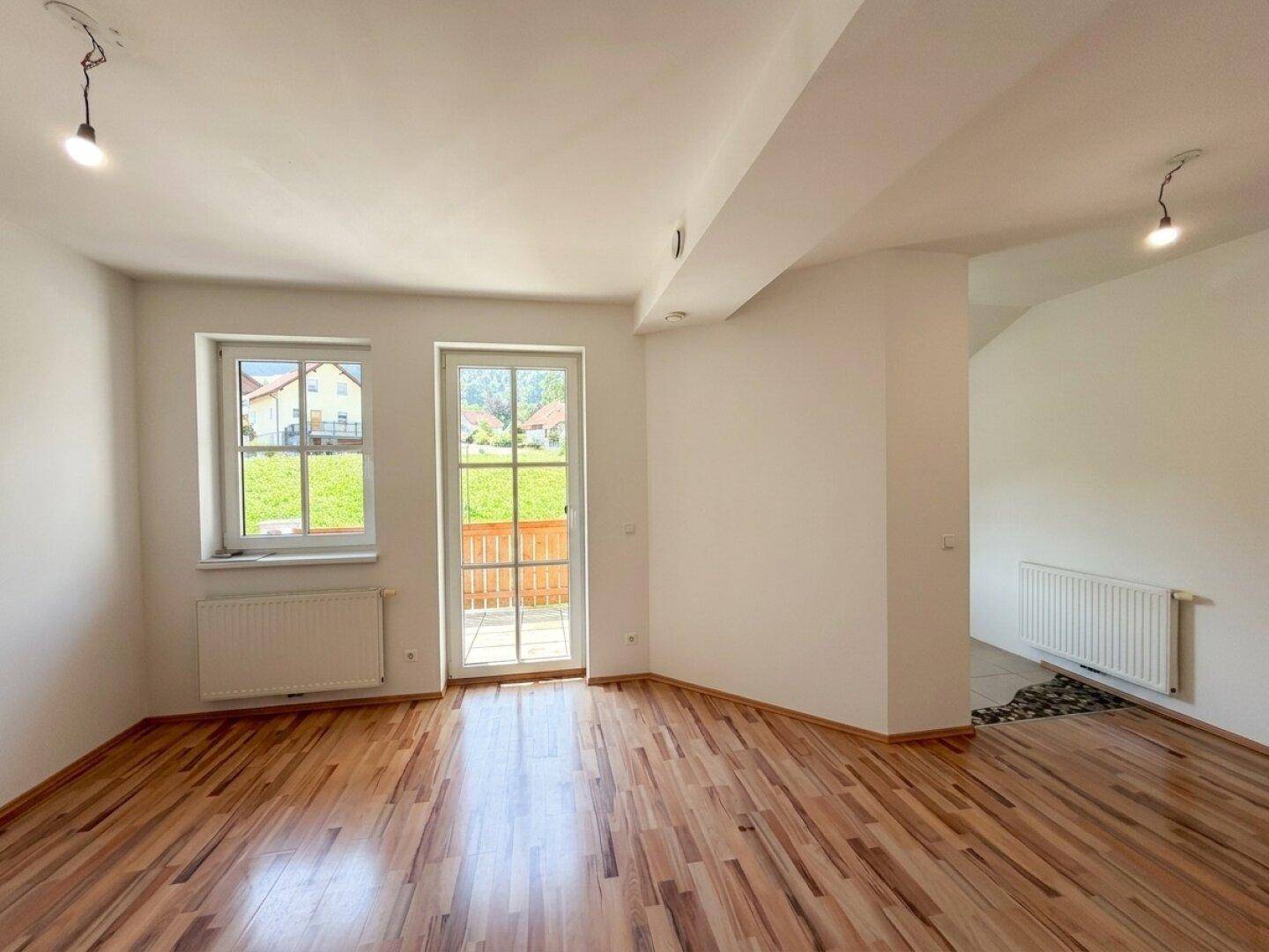 Helles, leeres Zimmer mit Laminatboden, weißen Wänden und Zugang zu einem Außenbereich.