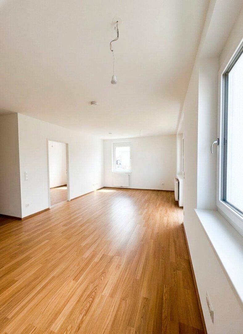Geräumiges, unmöbliertes Zimmer mit hellem Parkettboden und weiß gestrichenen Wänden.