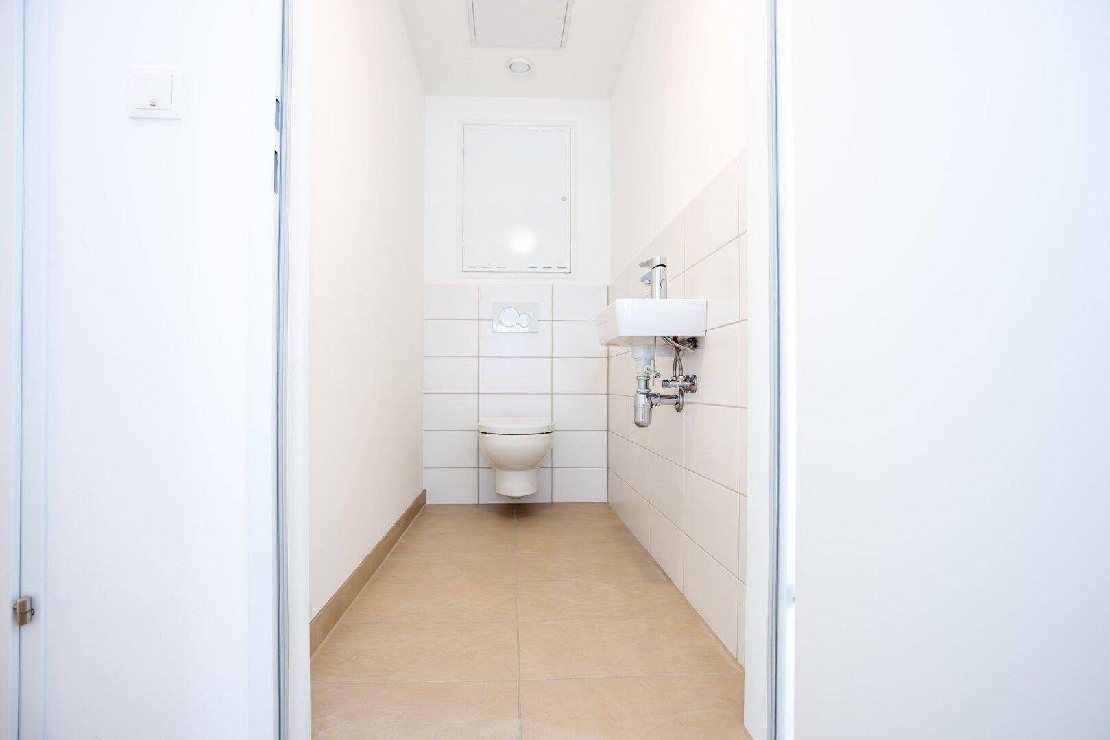 Funktionelles Gäste-WC mit wandhängender Toilette, kleinem Waschbecken und beigefarbenen Fliesen.