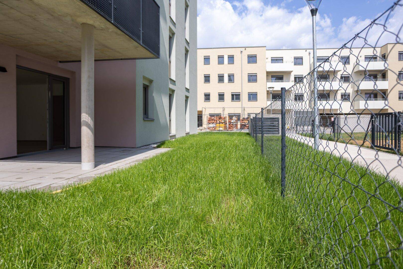 Gepflegte Rasenfläche neben einem modernen Wohngebäude mit Zugang zu einem Gehweg.